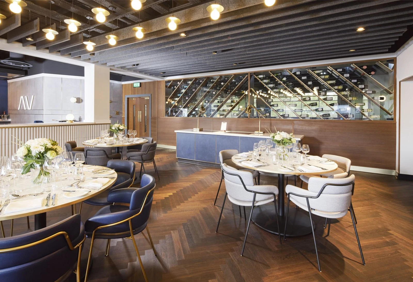 A bright dining room with warm wooden floors, comfortable seating, globe lights, and a diagonal wine display.